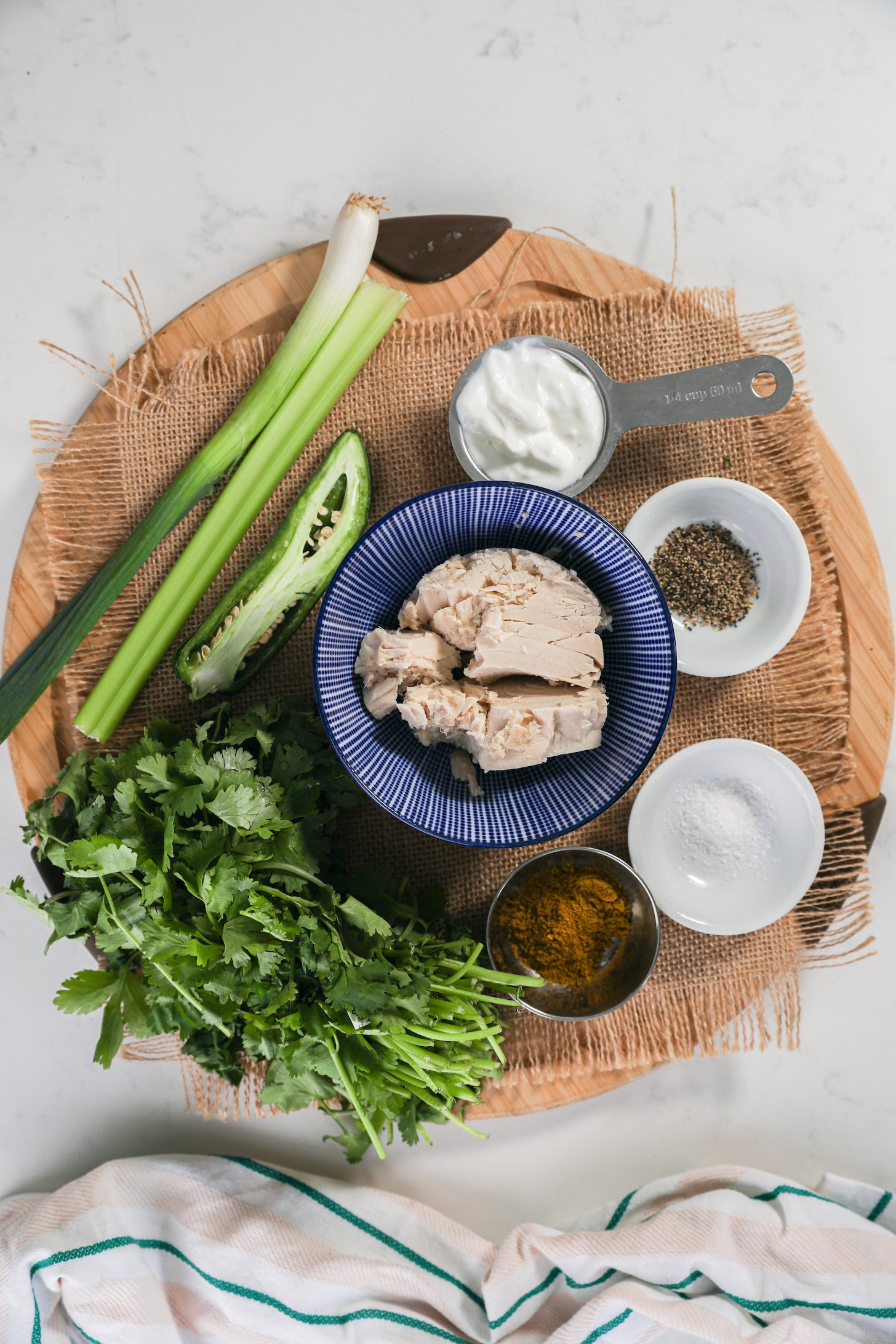 A collection of food ingredients, like canned fish, cilantro, celery, spring onion and spices displayed on a wooden board.