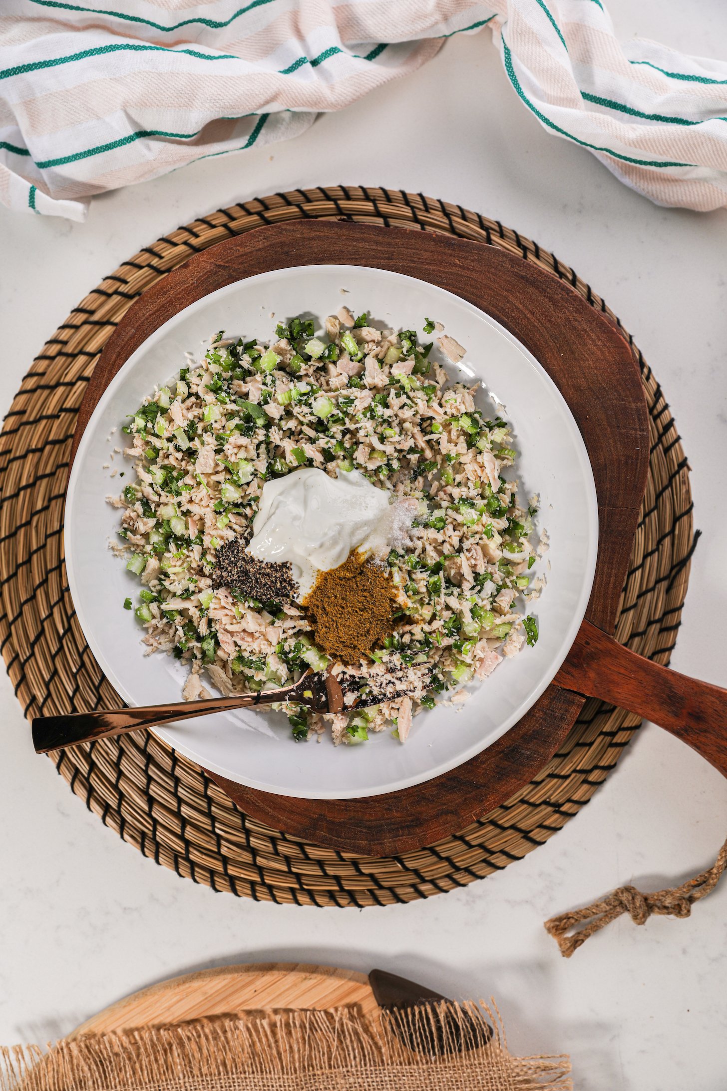 A bowl of minced fish with green vegetables topped with yogurt and spices.