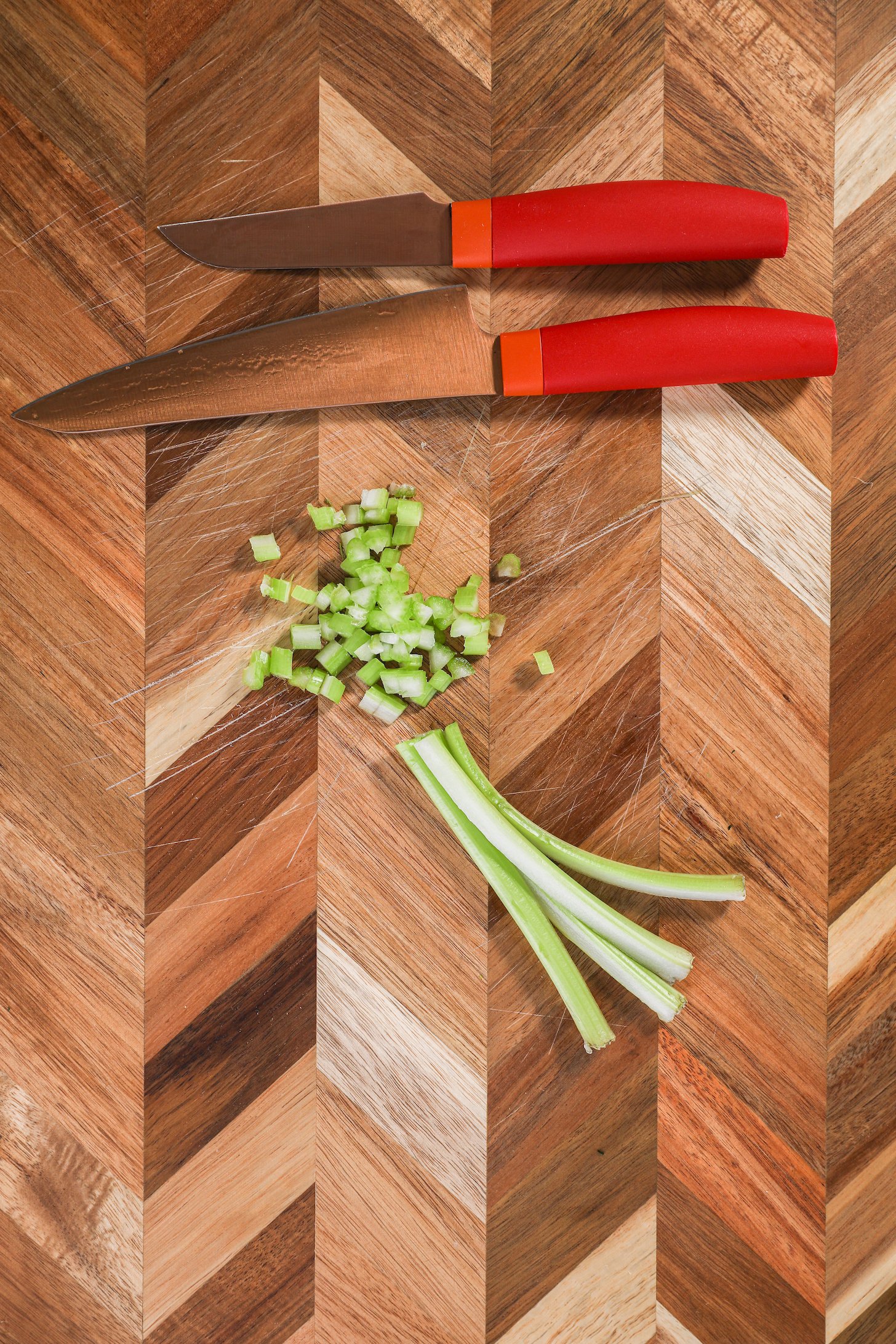 Chopped celery strips and small chunks next to a knife on a checkerboard style chopping board.