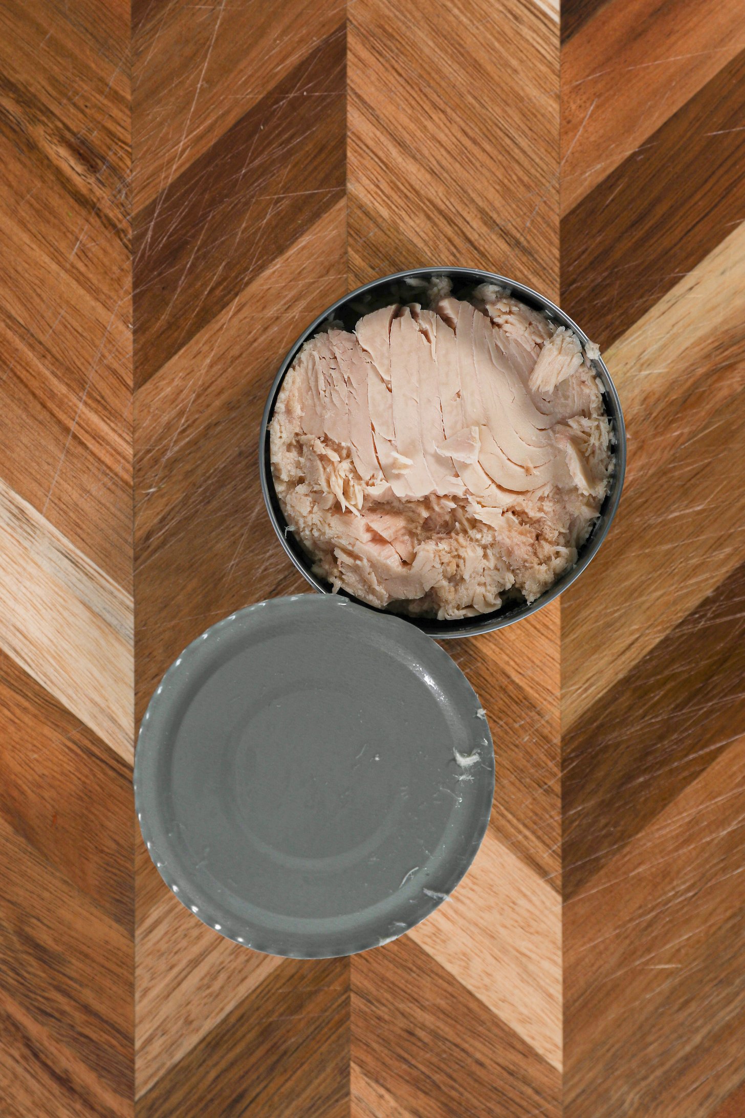 A opened can of tuna fish on a checkerboard style chopping board.