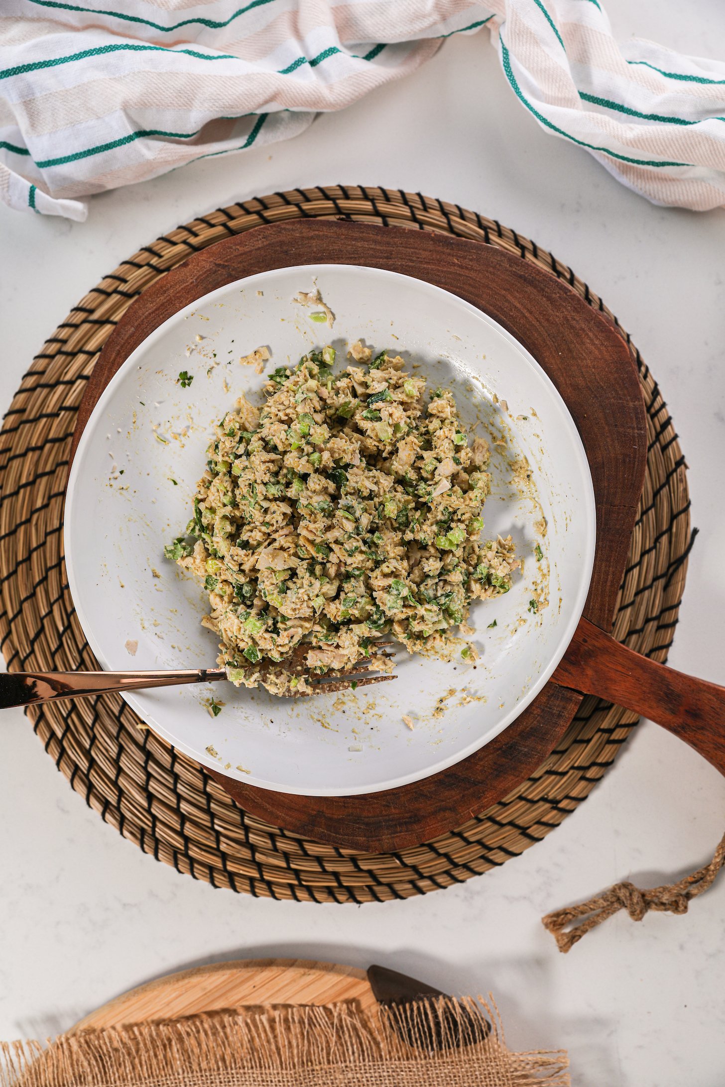 A bowl of mashed fish with green vegetable chunks with a fork that's displayed on a wooden board.