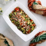 A rectangular bowl filled with chopped vegetables, beans and topped with almonds, styled around a decorative scarf.