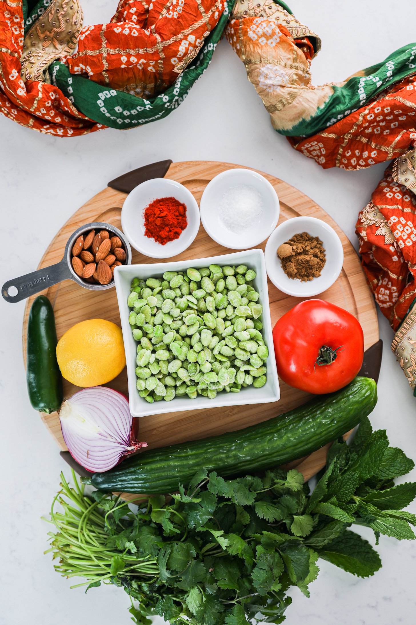 Top view of a collection of food ingredients including edamame, cucumber, herbs, tomato and nuts.