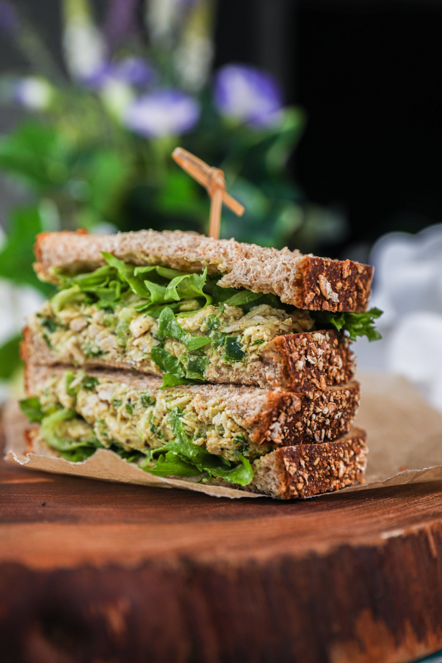 A side shot of a stack of two sandwiches filled with greens and white tuna with a pick inserted in them.