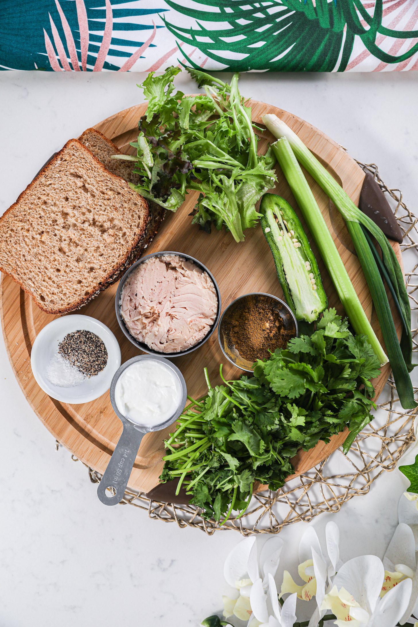 A collection of food ingredients like canned fish, greens, herbs, slices of bread and spices on a wound wooden board.