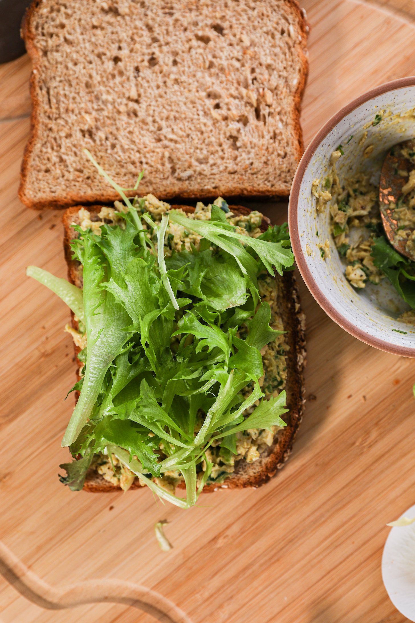 An open face sandwich topped with a heap of lettuce with a slice of bread next to it.