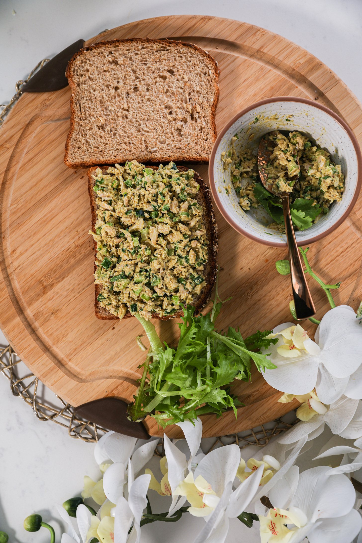 An open face sandwich topped with a fish and greens mixture with a wholegrain slice of bread next to it.